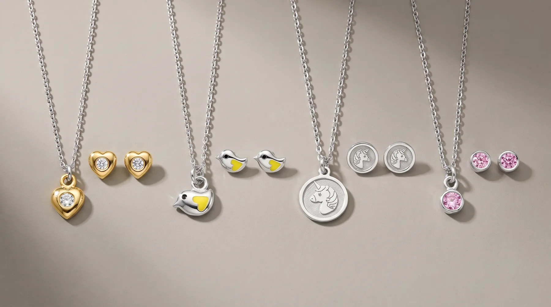 Five jewelry sets arranged in a row, each consisting of a pendant necklace and matching stud earrings in gold, silver, and rose gold finishes with heart, bird, coin, and gemstone designs.