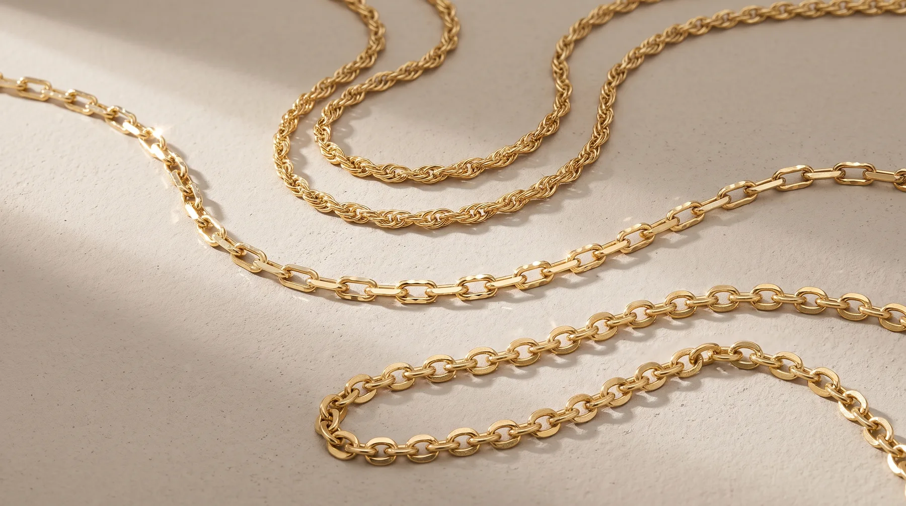 Five gold-toned chain necklaces of varying link styles arranged in loose coils on a beige surface.