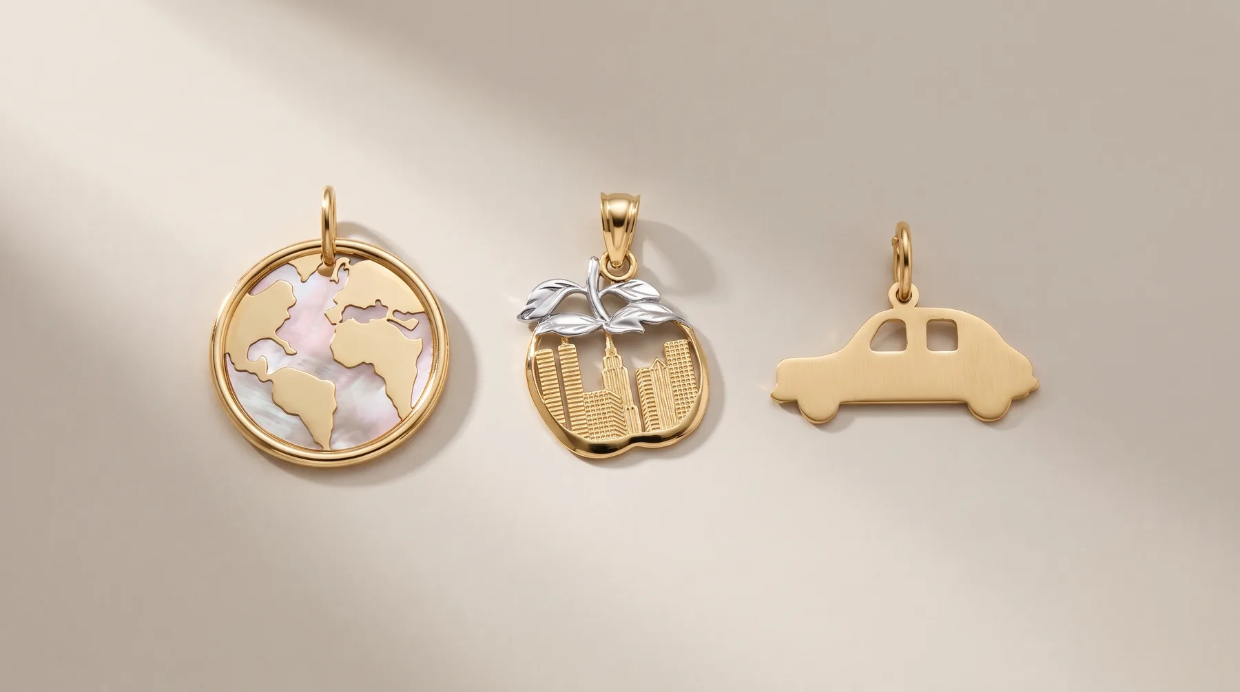 Three gold charms displayed on a light background: a circular pendant with mother-of-pearl continents, an apple-shaped charm with textured finish, and a car-shaped charm.