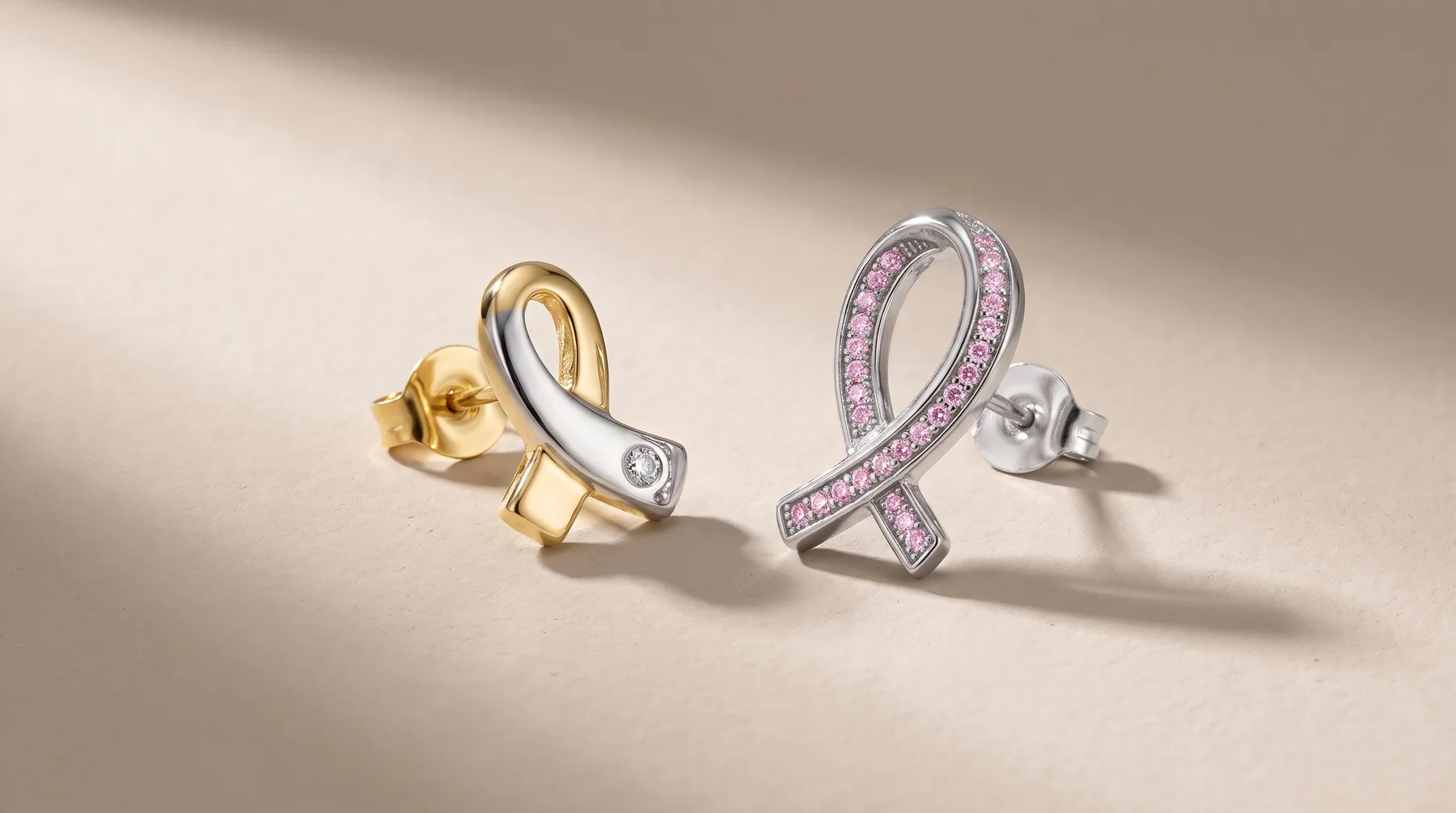 Two ribbon-shaped earrings with post backs sit on a neutral surface: one in gold with a diamond, the other in silver with purple stones.