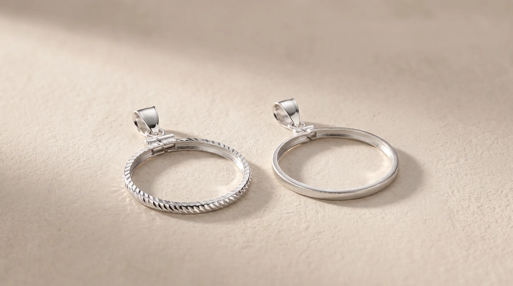 Two silver circular pendant frames with bail loops, one with a twisted rope texture around the edge and one plain, displayed on a neutral beige surface.
