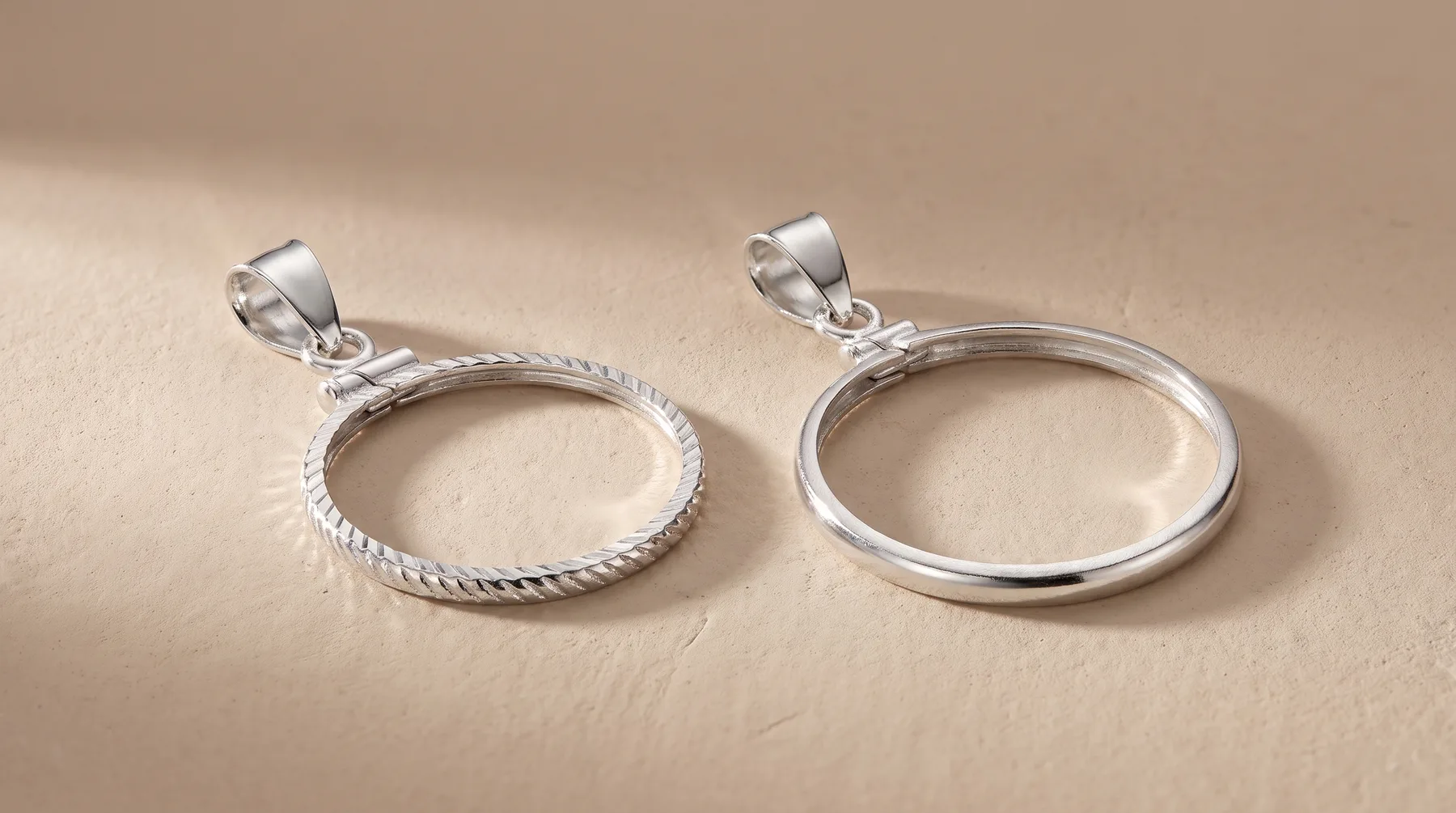 Two silver-toned circular pendant charms with loops, one featuring a twisted rope-textured edge and one with a smooth polished edge, displayed on a neutral beige surface.